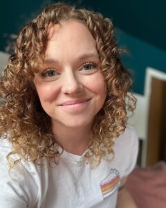 A wehite woman with curly brown hair smiling.