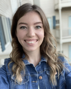 A smiling white woman with long brown hair, wearing a jean jacket.