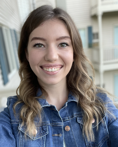 A smiling white woman with long brown hair, wearing a jean jacket.